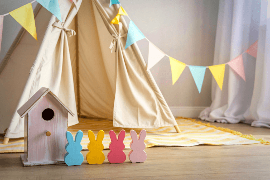 Πολύχρωμα ξύλινα λαγουδάκια μπροστά σε μια πάνινη σκηνη στο πάτωμα δωματίου.