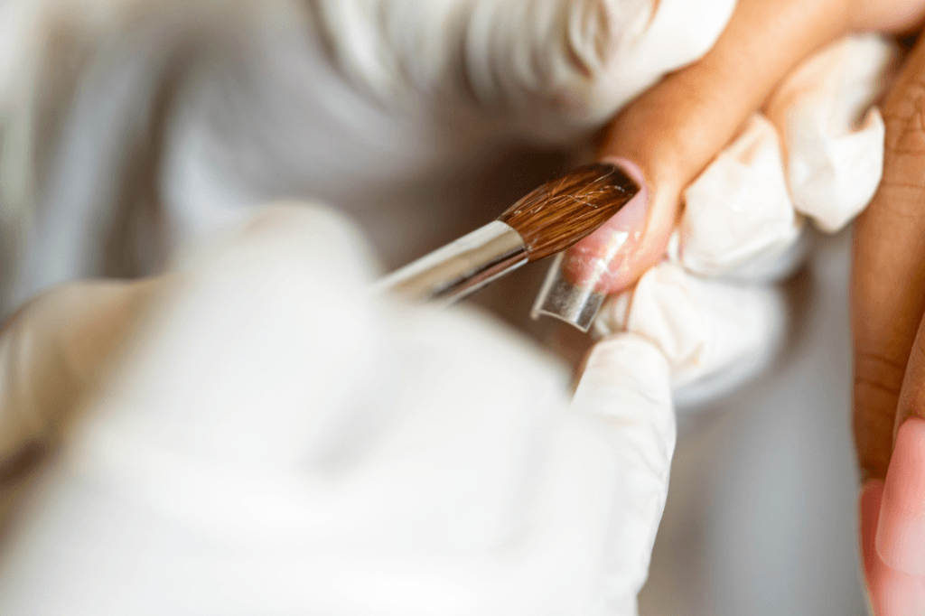 Επαγγελματίας βάφει με πινελάκι, ένα ακρυλικό νύχι σε γυναικείο δάκτυλο.