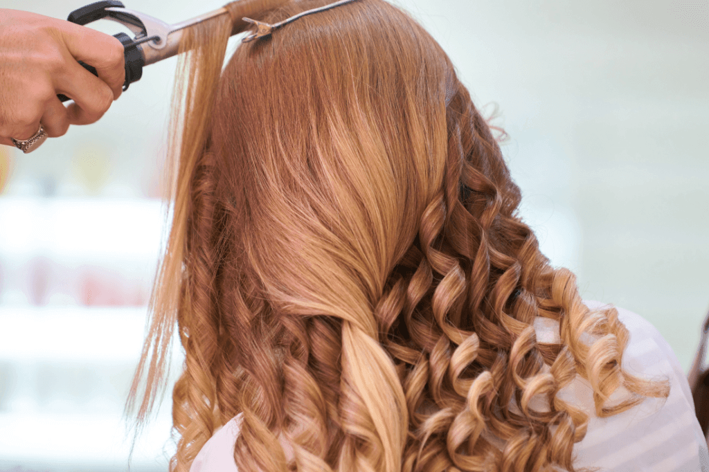 Επαγγελματίας με ειδικό ψαλίδι φτιάχνει μπούκλες σε γυναίκα με ξανθά μακριά μαλλιά.